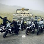 Grupo de motoristas con BMW R 1250 GS en el Cormet de Roselend, en los Alpes, rodeados de niebla y montañas.